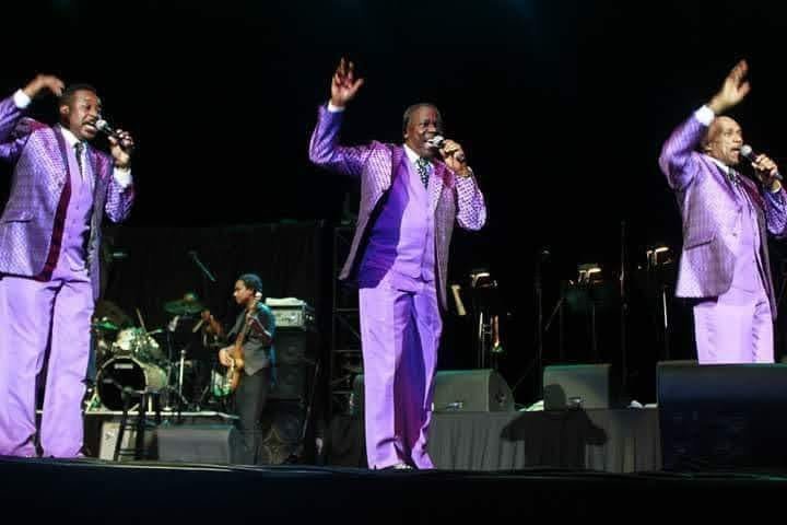 Performers in purple suits singing on stage