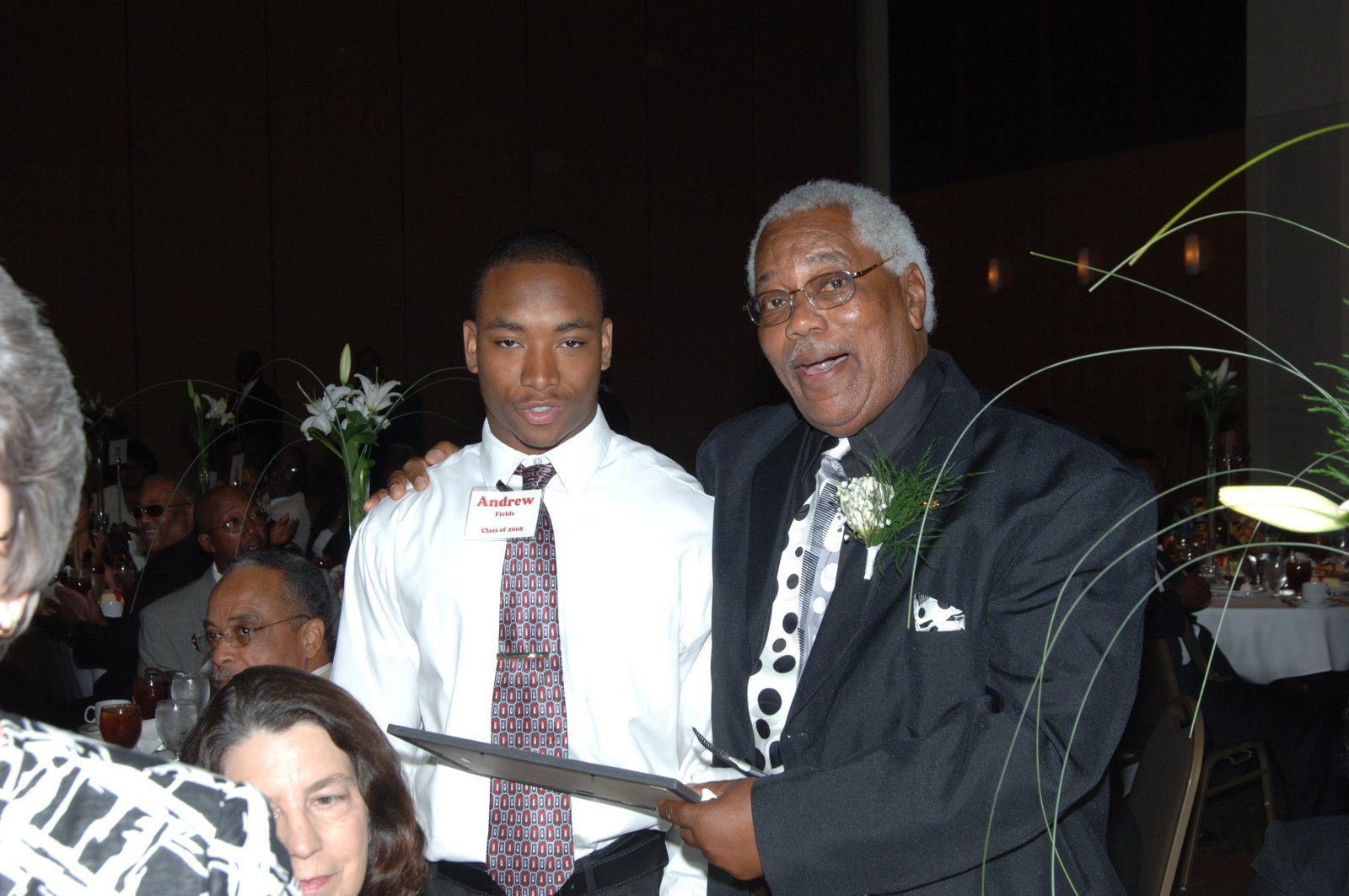 Alumni young man and older man at formal event with flowers and certificate