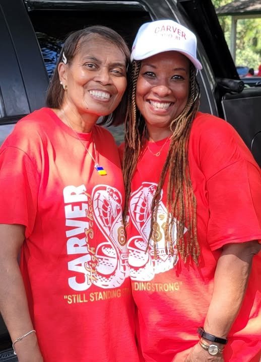Two alumni women in red Carver shirts at outdoor event