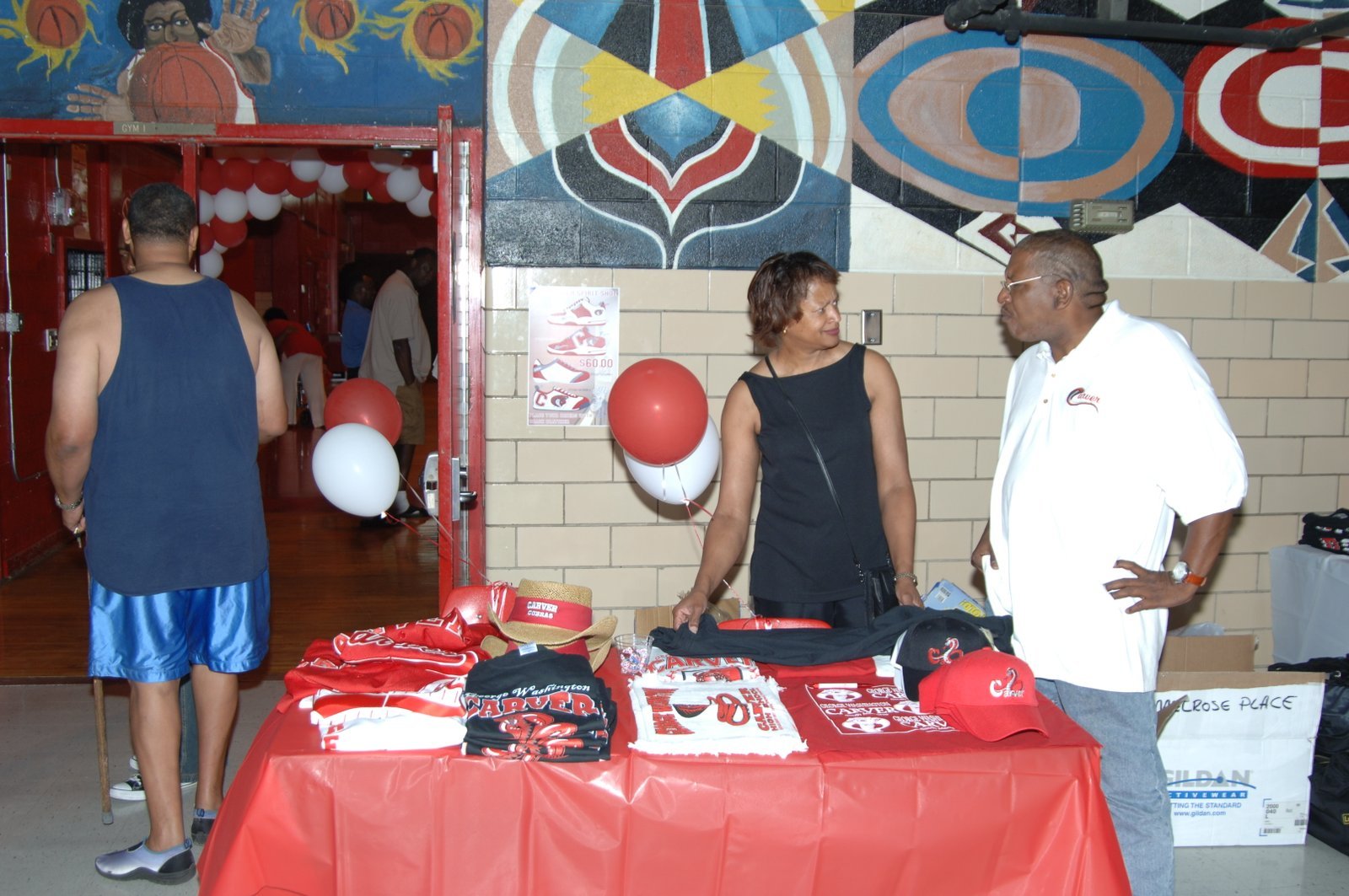 Alumni at school gymnasium event with merchandise table