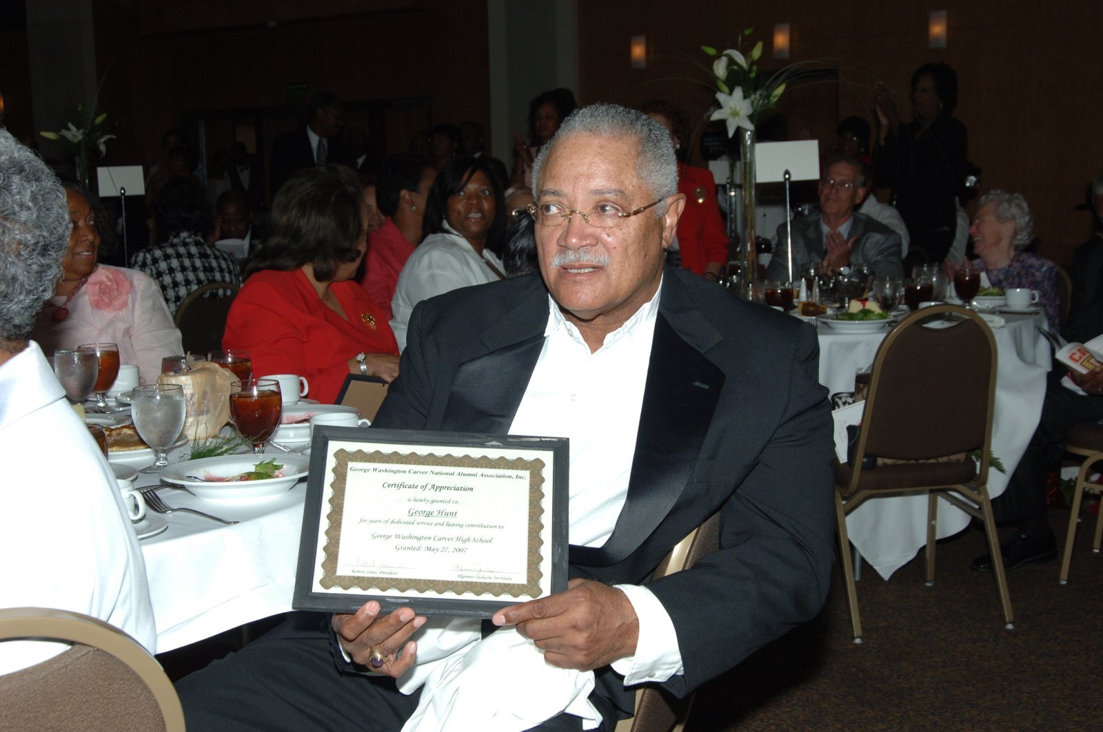 Alumni man at formal banquet event holding certificate of appreciation